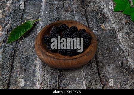 Minimalistisches horizontales Stillleben mit Kopierraum einer Holzschale mit Brombeeren auf einem alten Steinboden mit grünen Blättern Stockfoto