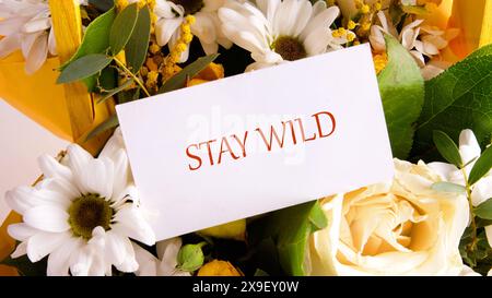 Finanzkonzept bedeutet „Stay Wild“ mit der Inschrift auf einer Visitenkarte, die in einem Blumenstrauß platziert ist. Stockfoto