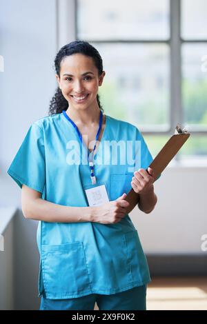Lächelnde Ärztin hält Clipboard im hellen Krankenhauskorridor Stockfoto