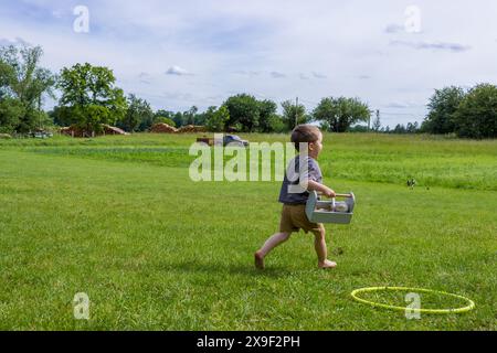 Blick von hinten auf den kleinen Jungen, der barfuß auf dem Gras im Dorf läuft Stockfoto