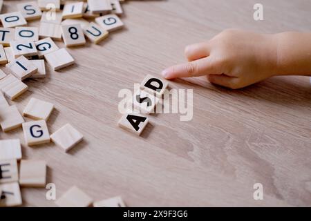 Hände aus der Nähe, kleines Kind 3 Jahre alt spielt hölzerne Alphabetblöcke, macht Wort ASD aus Buchstaben, frühzeitige Diagnose und Intervention, Unterstützung für Menschen Stockfoto