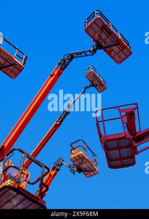 Große Gruppe von Gelenkkranen, Körben und hydraulischen Armen hoch in einem klaren blauen Himmel, Perspektive aus flachem Winkel. Stockfoto