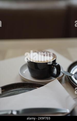 Cappuccino heißer Kaffee, schwarze Tasse Schlagsahne in luxuriösem Café-Kopfschuss mit geringer Schärfentiefe. Stockfoto