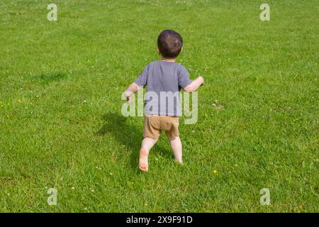 Blick von hinten auf den kleinen Jungen, der barfuß auf dem Gras im Dorf läuft Stockfoto