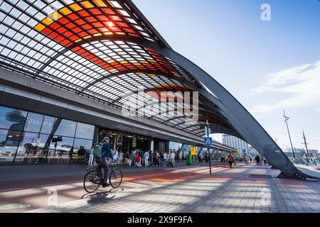 Radfahrer, die am 26. Mai 2024 unter dem farbenfrohen rot-orangen Dach des Amsterdamer Centraal-Bahnhofs in den Niederlanden abgebildet wurden. Stockfoto