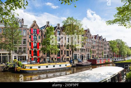 Hübsche Stadthäuser mit farbenfrohen Fensterläden säumen die Prinsengracht, die voll von vertäuten Bootshäusern in Amsterdam, den Niederlanden, ist Stockfoto