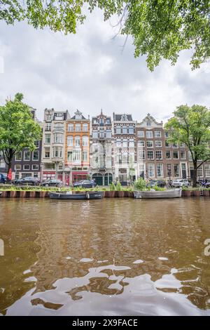 Ein typischer Blick auf farbenfrohe, dünne und hohe Kanalhäuser, die die Prinsengracht säumen und teilweise von Bäumen eingerahmt sind. Gesehen am 29. Mai 2024 in Amsterdam, Stockfoto