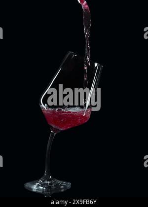 Rotwein wird in ein anliegendes Weinglas mit schiefem Stiel gegossen Stockfoto