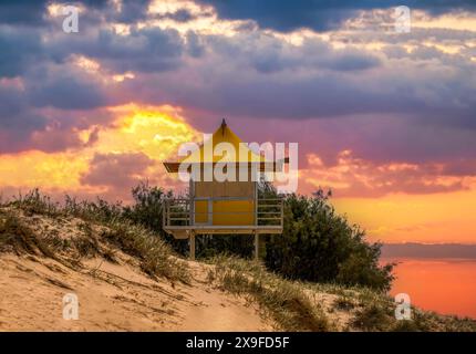 Dramatischer Sonnenuntergang über einer Rettungshütte in Sanddünen an einem Strand, Queensland, Australien Stockfoto