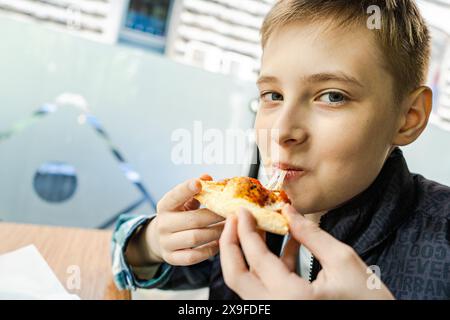 Porträt eines lächelnden Jungen, der in einem Straßencafé eine Pizza mit Peperoni, Oliven und Jalapeno isst Stockfoto