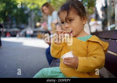 Baby-Mädchen, das Eiseis zum ersten Mal im Sommer in der Stadt probiert. Glückliches Kleinkind, das Eis im Freien in der europäischen Stadt isst Stockfoto