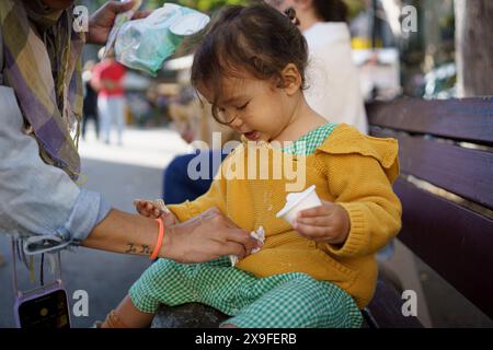 Baby-Mädchen, das Eiseis zum ersten Mal im Sommer in der Stadt probiert. Glückliches Kleinkind, das Eis im Freien in der europäischen Stadt isst Stockfoto