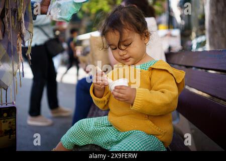 Baby-Mädchen, das Eiseis zum ersten Mal im Sommer in der Stadt probiert. Glückliches Kleinkind, das Eis im Freien in der europäischen Stadt isst Stockfoto