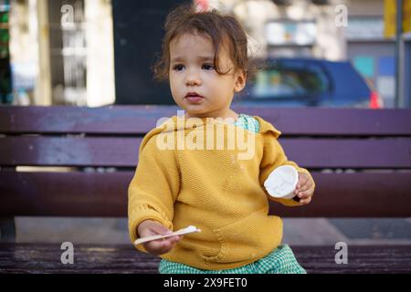 Baby-Mädchen, das Eiseis zum ersten Mal im Sommer in der Stadt probiert. Glückliches Kleinkind, das Eis im Freien in der europäischen Stadt isst Stockfoto