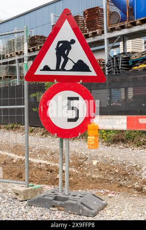 Baustelle mit Schotterstraße, einem Geschwindigkeitsbegrenzungsschild mit 5 km/h und einem Schild zur Baustelle, neben anderen Warnschildern. Stockfoto