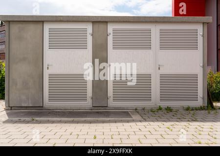 Modernes Transformatorhaus mit verschlossenen Aluminiumtüren. Tagesaufnahme. Schatten auf dem Bürgersteig vorne. Stockfoto