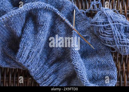 Nahaufnahme eines blauen isländischen Wollstrickpullovers auf den Metallnadeln mit Garnkugel Stockfoto