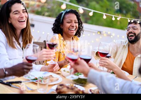 Treffen von fröhlichen jungen Freunden, die mit rotem Weinglas tosten, feiern Sommerparty auf der Terrasse. Stockfoto