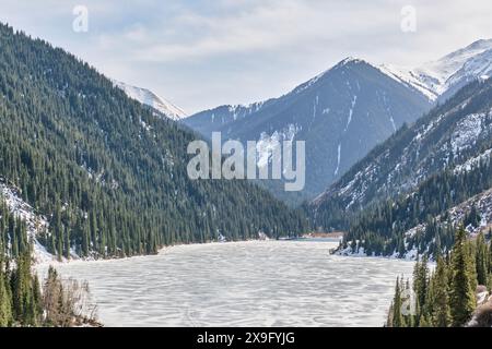 Der malerische Kolsai-See ist eisbedeckt, umgeben von grünen Hügeln. Nördlicher Tien Shan, Kolsai-Schlucht, Kasachstan. Frühlingslandschaft Stockfoto