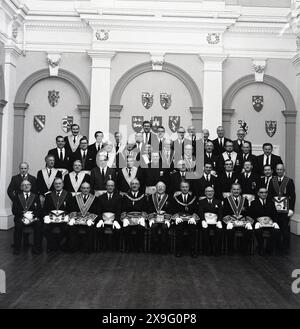 1960er Jahre, historisch, Gruppe von Maurern oder Freimaurern in Gewändern versammelte sich für ein Foto in der Halle einer Freimaurerloge in England, Großbritannien. Die Maurerbruderschaft stammt hunderte von Jahren aus den örtlichen Steinmetzgilden und ist eine brüderliche Gesellschaft, in der die Mitglieder einen Eid schwören, sich gegenseitig zu unterstützen und diese Unterstützung geheim zu halten, es sei denn, sie haben das Gesetz gebrochen. Stockfoto