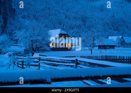 Die Nacht kommt, altes Haus mit Schnee bedeckt auf dem Hintergrund des Waldes Stockfoto