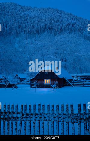 Die Nacht kommt, altes Haus mit Schnee bedeckt auf dem Hintergrund des Waldes Stockfoto
