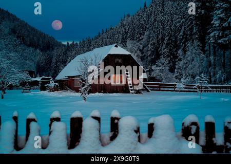 Die Nacht kommt, altes Haus mit Schnee bedeckt auf dem Hintergrund des Waldes Stockfoto