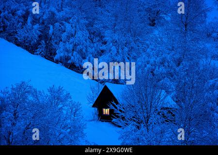 Die Nacht kommt, altes Haus mit Schnee bedeckt auf dem Hintergrund des Waldes Stockfoto