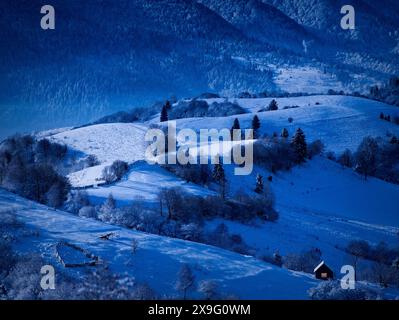 Die Nacht kommt, altes Haus mit Schnee bedeckt auf dem Hintergrund des Waldes Stockfoto