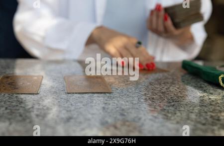 Montenegro, Budva, 6. Mai 2024. Frau mit roten Nägeln und weißer Bluse, die Tarotkarten auf Granittisch legt, grüne Samttasche sichtbar. Stockfoto