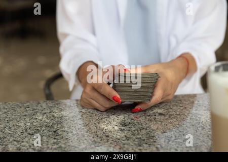 Frau mit roten Nägeln und weißer Bluse, die einen Stapel Tarotkarten an einem Granittisch in einem Café hält. Kopierbereich. Stockfoto