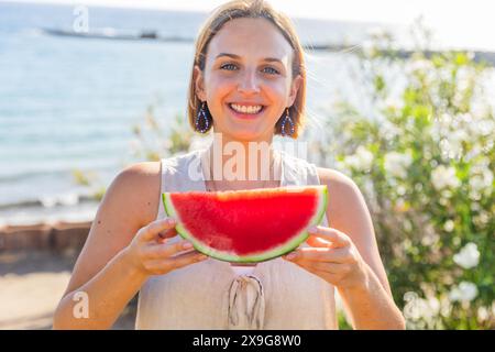 Eine Frau hält eine Wassermelonenscheibe in der Hand und lächelt in die Kamera. Stockfoto