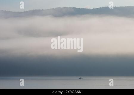 Fischerboot in der Inside Passage im Südosten Alaskas, unter niedrigen Wolken mit hohen Bergen, die vom Tongass National Forest bedeckt sind Stockfoto