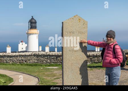 Ein Tourist weist auf eine Markierung am Dunnet Head in Nordschottland hin, die den nördlichsten Punkt des schottischen Festlandes und der Insel Großbritannien darstellt. Stockfoto