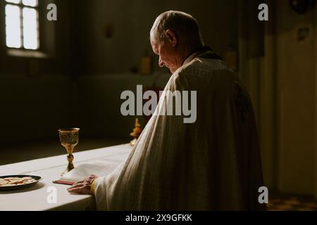 Unauffälliger Schuss eines älteren kaukasischen katholischen Priesters, der sich auf den heiligen Kommunionritus in der Kirche vorbereitet, Kopierraum Stockfoto