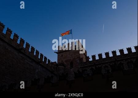 Die Flagge der valencianischen Gemeinde weht während des Las fallas Festivals auf einem historischen Gebäude mit Zinnen vor einem klaren blauen Himmel Stockfoto