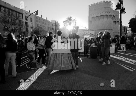 Allera in traditioneller Kleidung spaziert durch die Menge in der Nähe der Serranos-Türme und genießt die lebhafte Atmosphäre der Las fallas-Feste bei Sonnenuntergang Stockfoto
