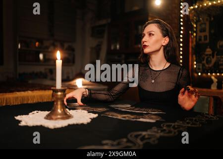 Porträt eines rätselhaften Wahrsagers, der Tarotkarten auslegt, Zeichen auf Zauberkarten liest und mit einem Kunden spricht, der im Dunkeln am Tisch sitzt Stockfoto