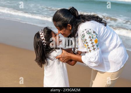 Eine liebevolle Mutter und ihre Tochter gehen Hand in Hand am Sandstrand entlang und genießen den warmen Sonnenuntergang. Stockfoto