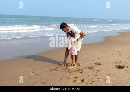 Vater und Tochter schaffen Erinnerungen, indem sie im Sand an einem ruhigen Strand spielen. Stockfoto