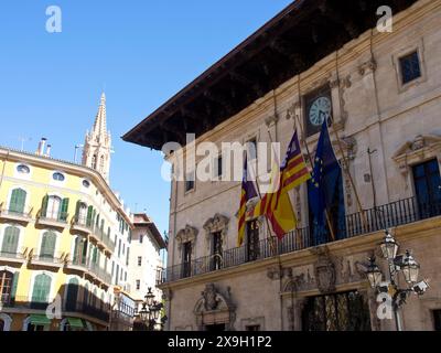 Historisches Gebäude mit verschiedenen Flaggen und einem Uhrenturm auf einem belebten Platz unter klarem Himmel, palma de Mallorca am Mittelmeer mit seinen Stockfoto