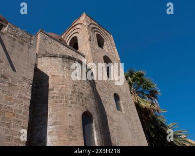 Historisches Kirchengebäude mit runden Türmen und Palmen in der Sonne, palermo in sizilien mit einer beeindruckenden Kathedrale, Denkmälern und alten Häusern Stockfoto