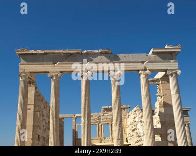 Antike Ruinen mit Säulen und teilweise erhaltenes Gebäude unter einem klaren blauen Himmel, altes Gebäude mit Säulen und Bäumen auf der Akropolis in Stockfoto