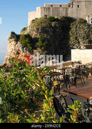 Terrasse mit Stühlen und Tischen neben einer Felsformation mit Meerblick und historischer Festung, Altstadt von Dubrovnik mit historischen Häusern Stockfoto