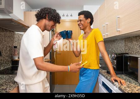 Glückliches Schwulenpaar, das Kaffee genießt und morgens zu Hause auf das Handy schaut Stockfoto
