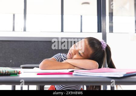 Ein birassisches Mädchen mit langen dunklen Haaren legt ihren Kopf auf den Armen in einem Klassenzimmer, Kopierraum Stockfoto