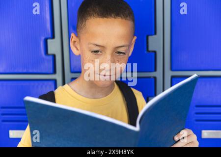 In einer Schule steht ein junger birassischer Junge vor einem blauen Spind Hintergrund Stockfoto