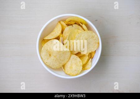 Eine Schüssel knuspriger Kartoffelchips auf hölzernem Hintergrund. Blick von oben auf knusprige köstliche Kartoffelchips, klassisches gesalzenes Aroma. Stockfoto