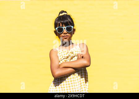 Ein birassisches Mädchen, das eine Sonnenbrille und ein Sommerkleid trägt, posiert selbstbewusst im Freien Stockfoto