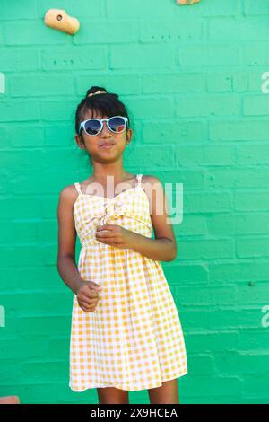 Ein birassisches Mädchen, das Sonnenbrille und Sommerkleid trägt, posiert selbstbewusst im Freien Stockfoto